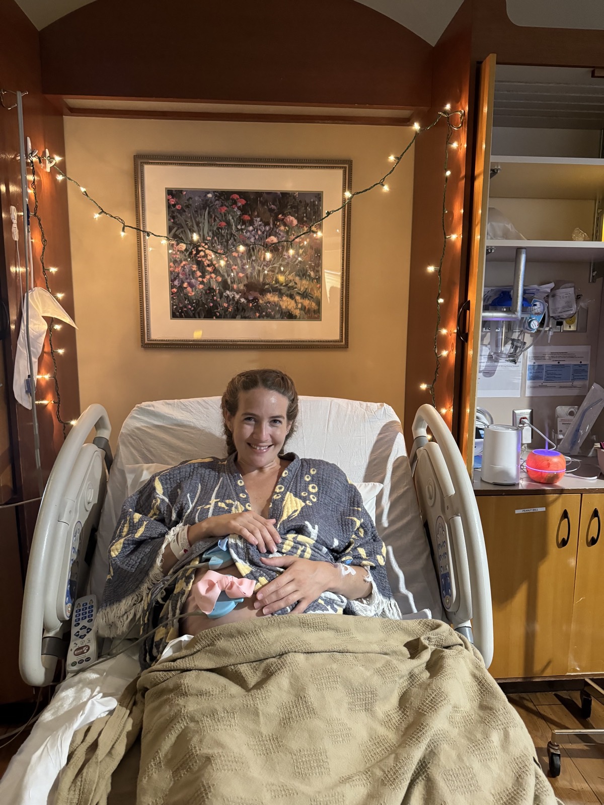 A mother resting in a Charlotte hospital bed holding her newborn, with string lights hung around the room.