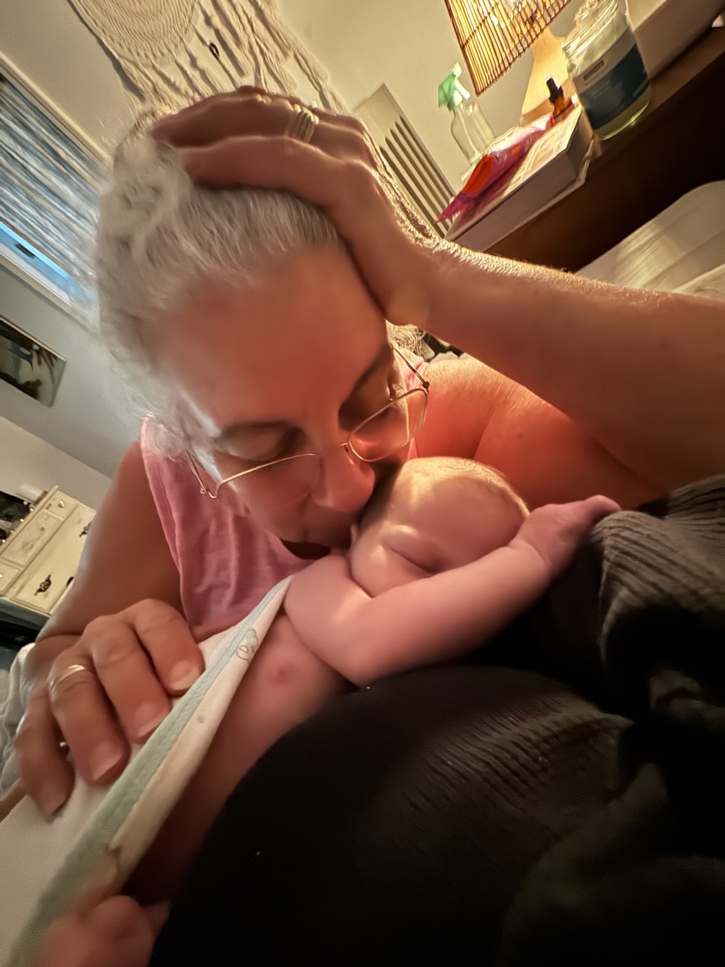 A grandmother kissing the head of her sleeping newborn grandchild.