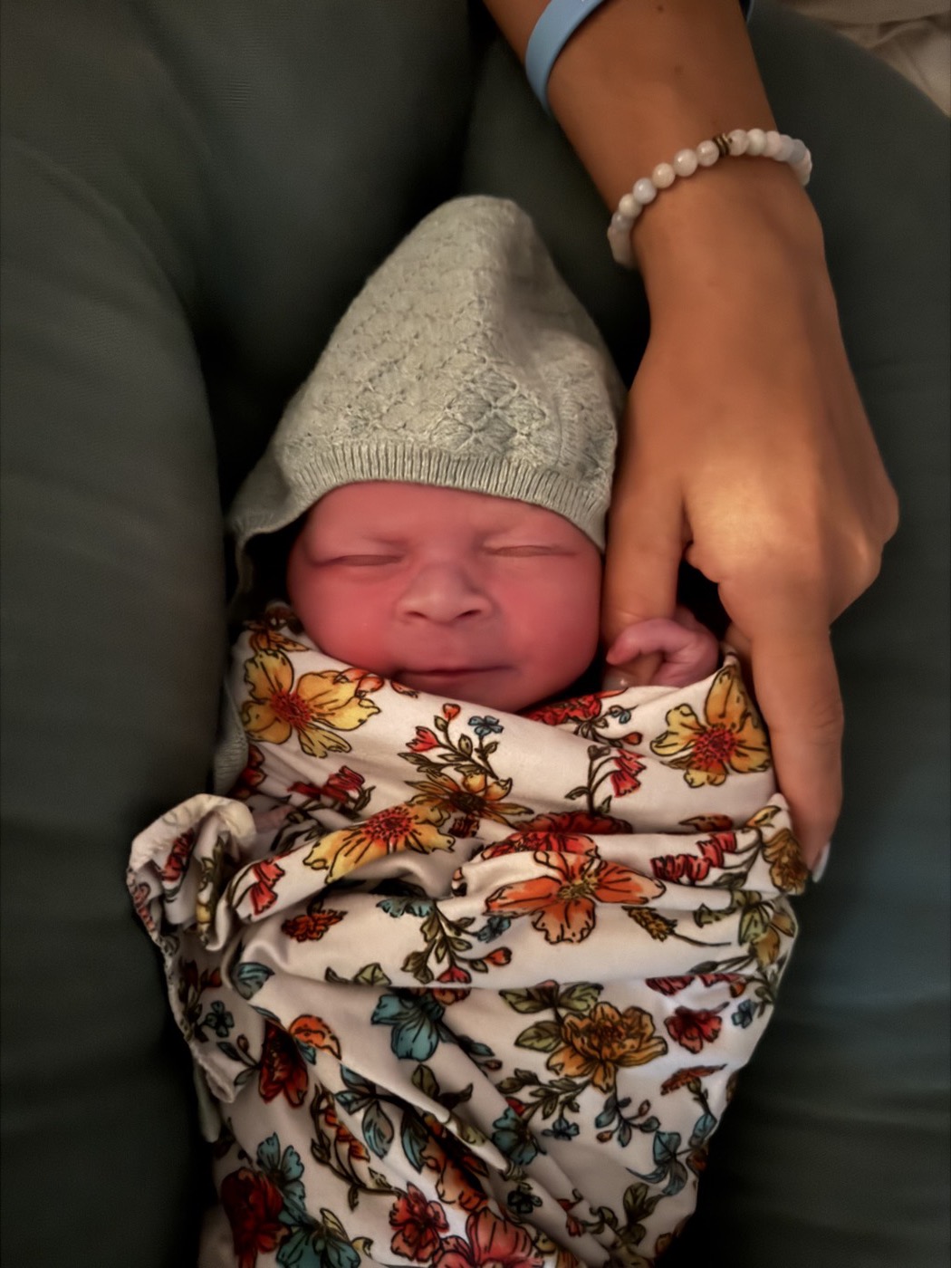 A newborn baby swaddled in a floral wrap, sleeping in her mother's arms.